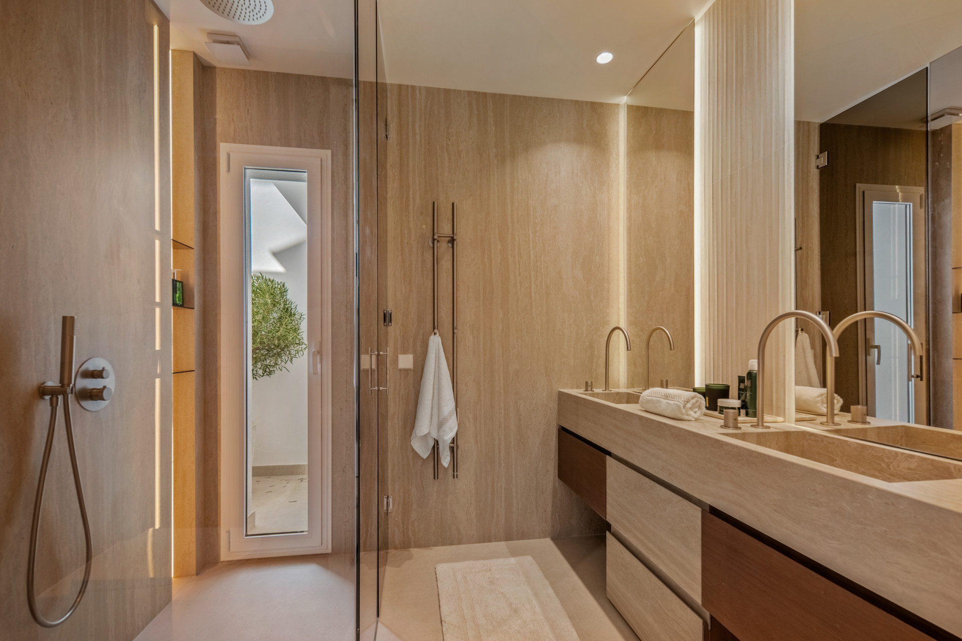 Warm wood cabinetry and twin basins beside a glass shower and tall window.