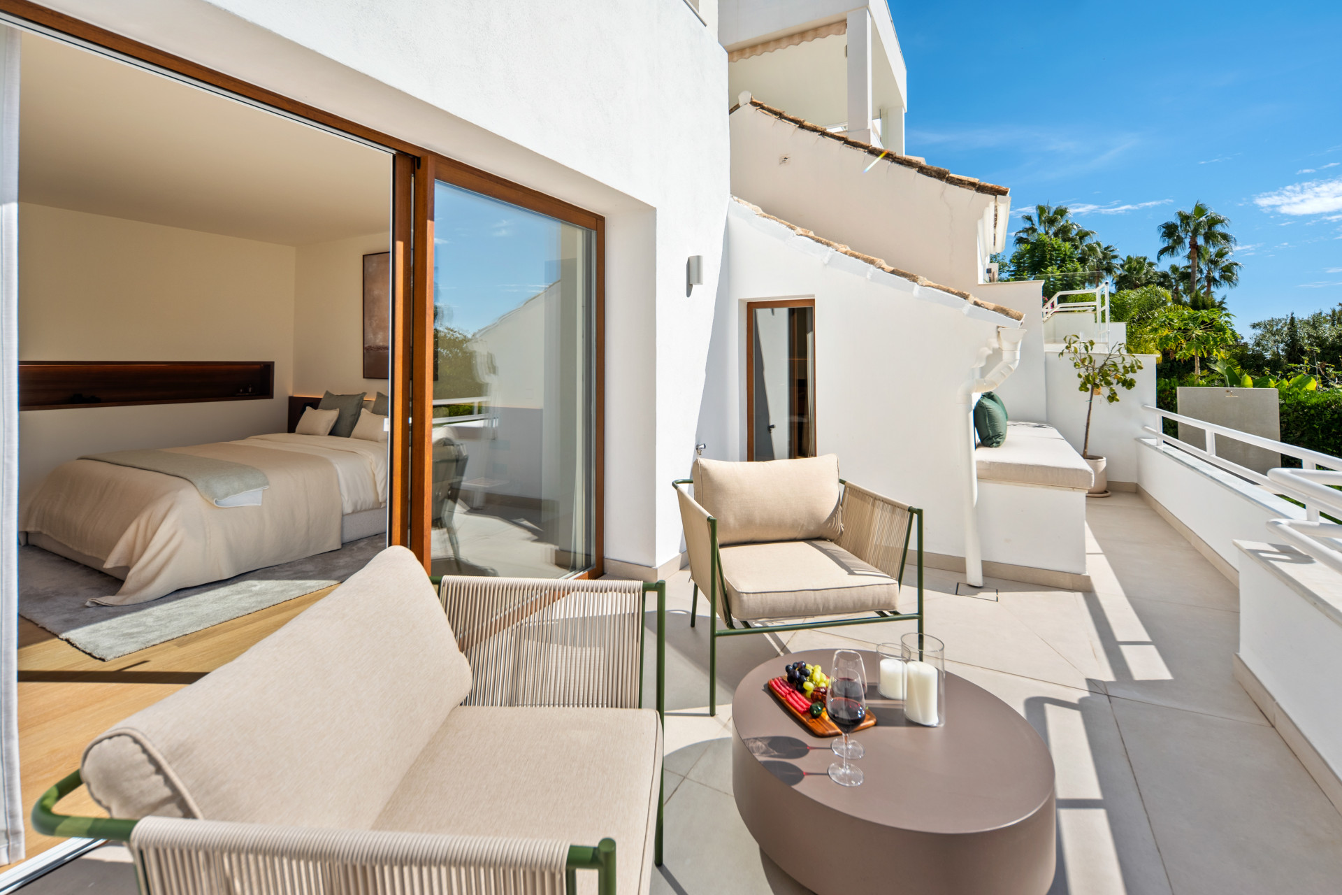 Outdoor seating on a sunny terrace beside open bedroom doors.