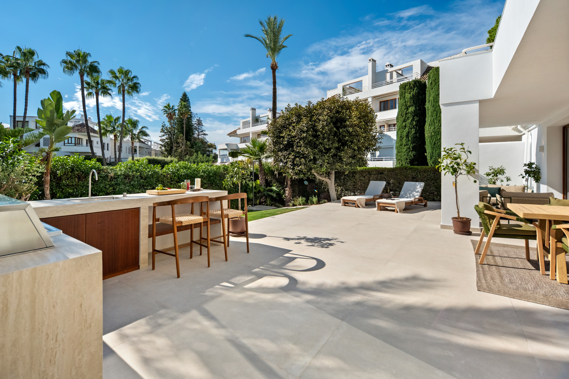 Spacious ground-floor terrace with an outdoor kitchen, dining area and garden beyond.
