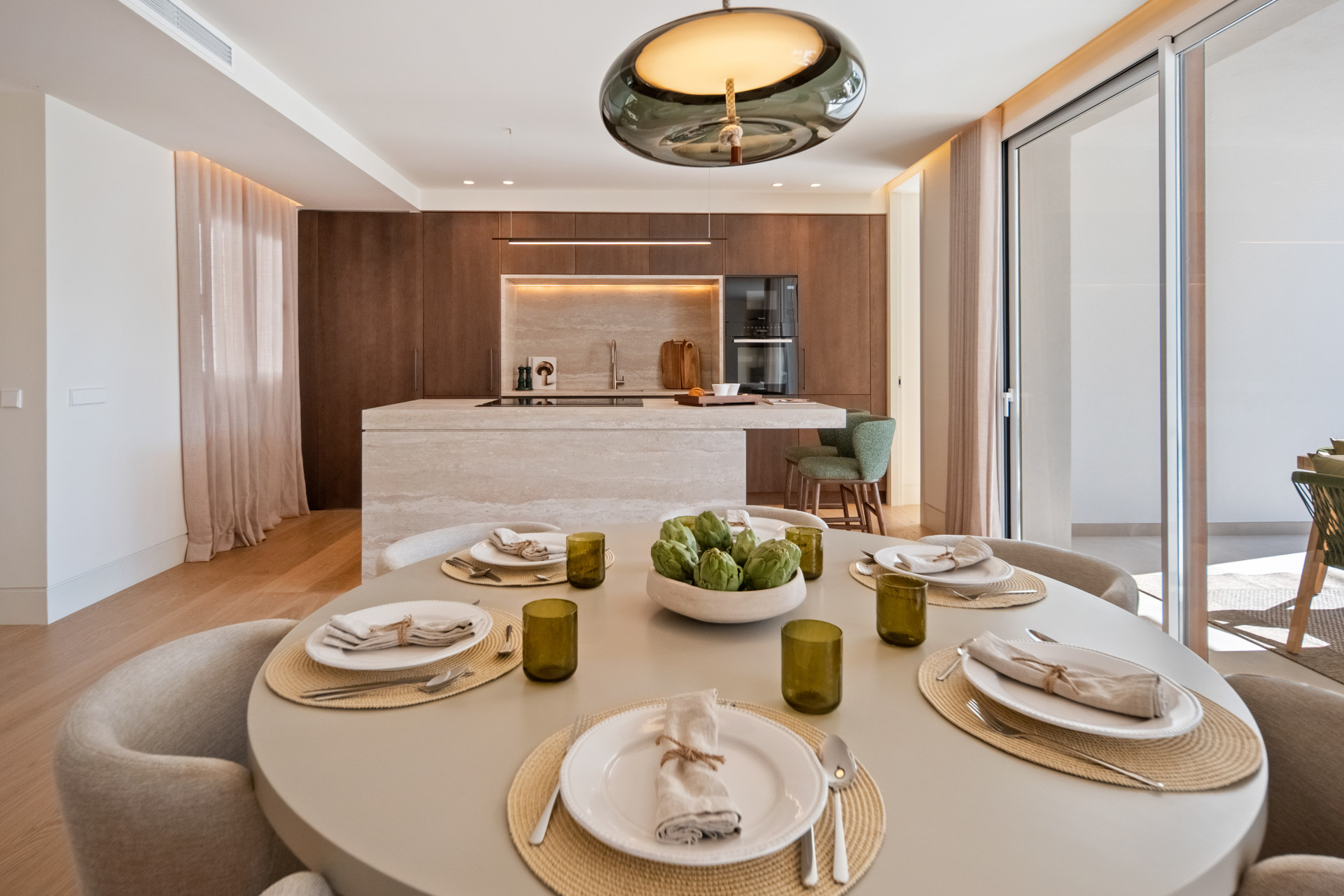 Round dining table in front of a stone kitchen island and wood cabinetry.