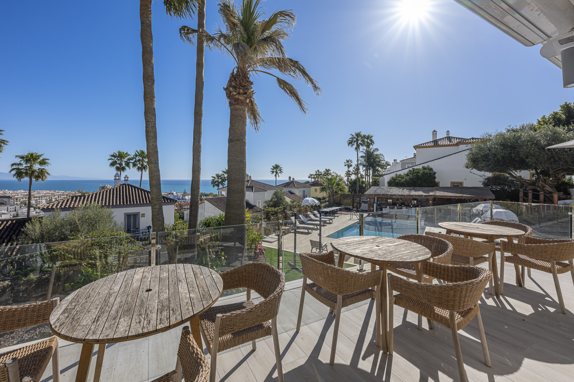 Dining tables on a glazed-balustrade terrace overlooking the pool, neighbouring rooftops and the Mediterranean.