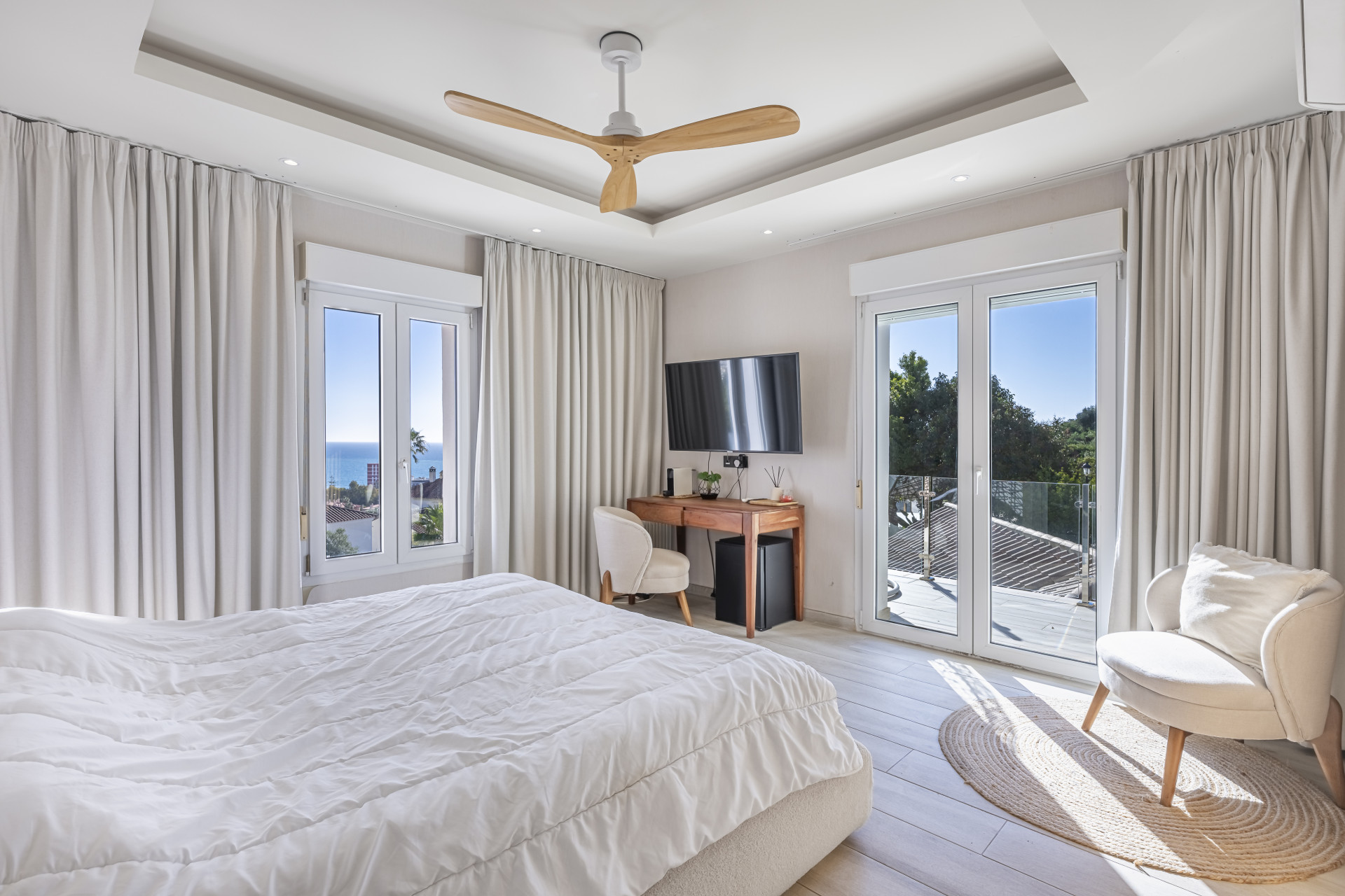 Bright bedroom with a ceiling fan, sea-facing window and glazed door opening to a balcony.