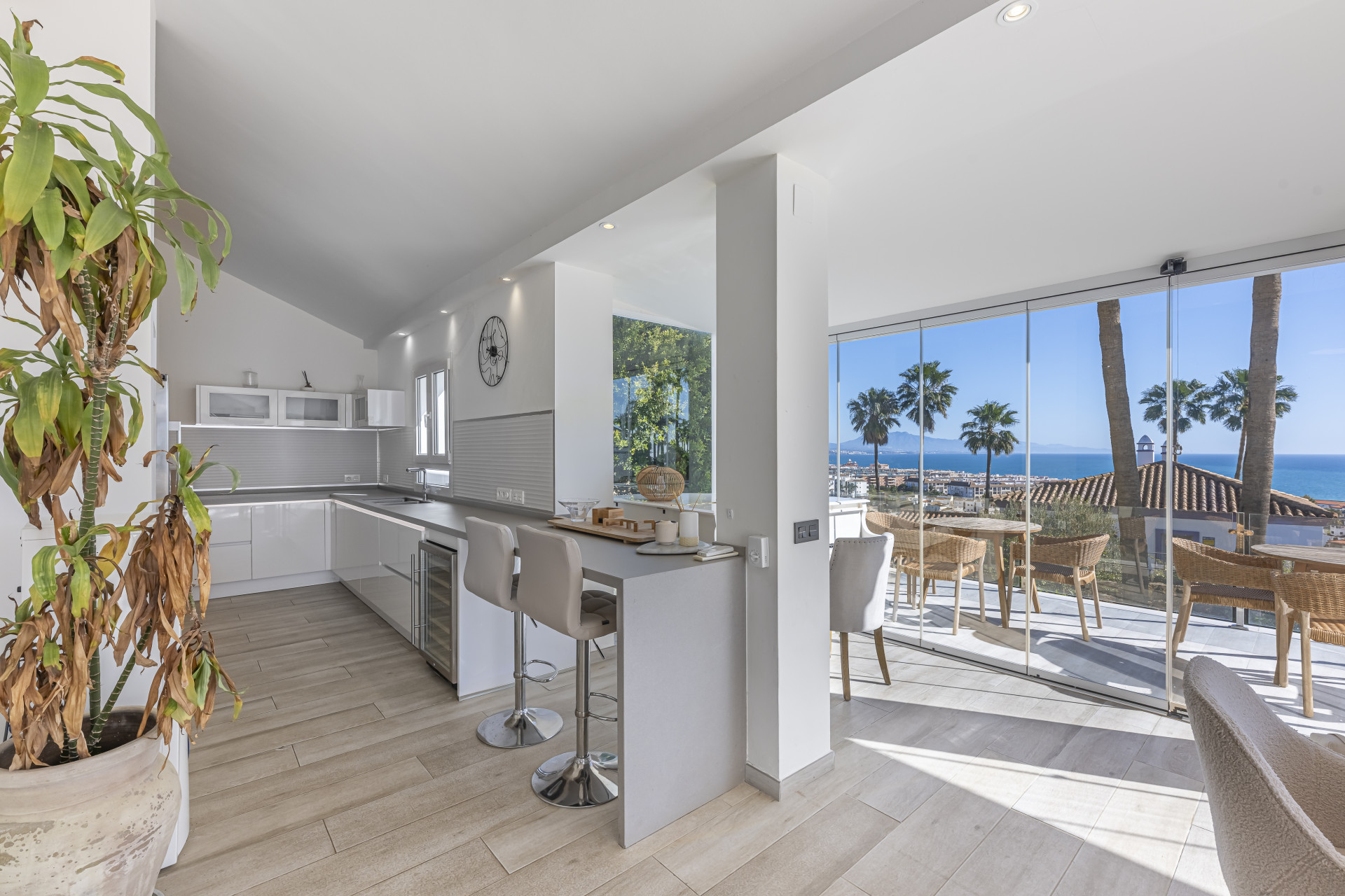 White kitchen and breakfast counter beside glazing opening onto a sea-view dining terrace.