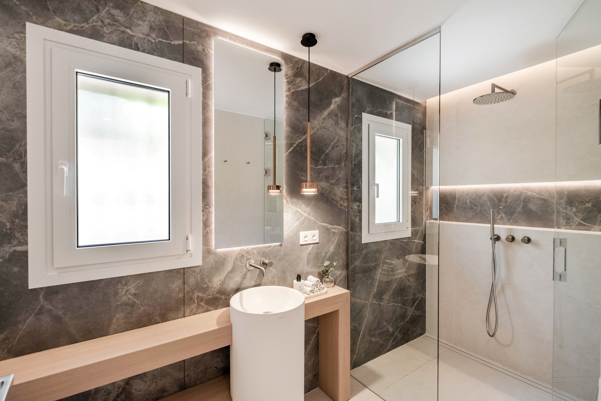 Walk-in shower, stone surfaces and a round basin in a bathroom.
