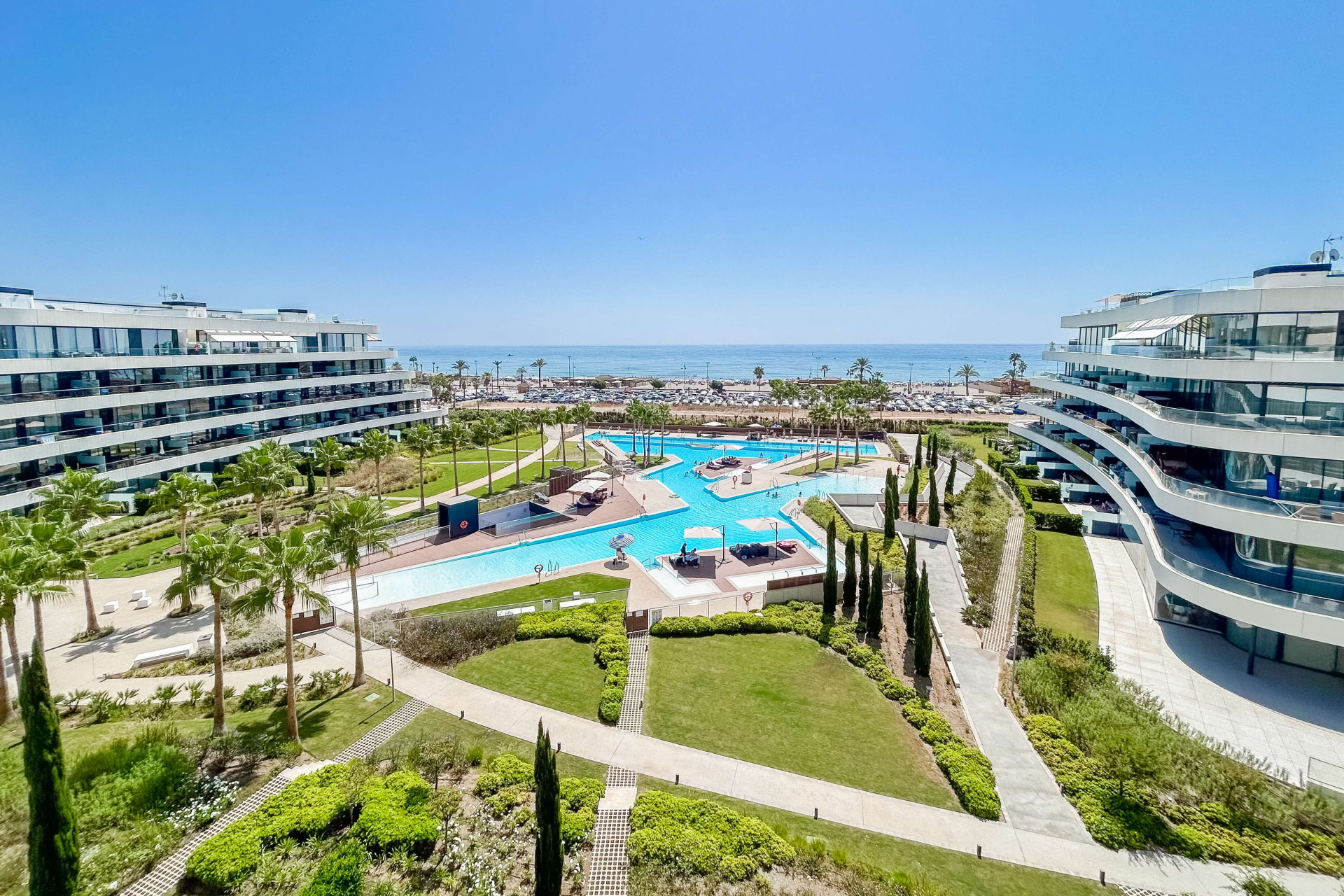 Curved apartment buildings framing communal gardens, swimming pools and a sea view at Nereidas.