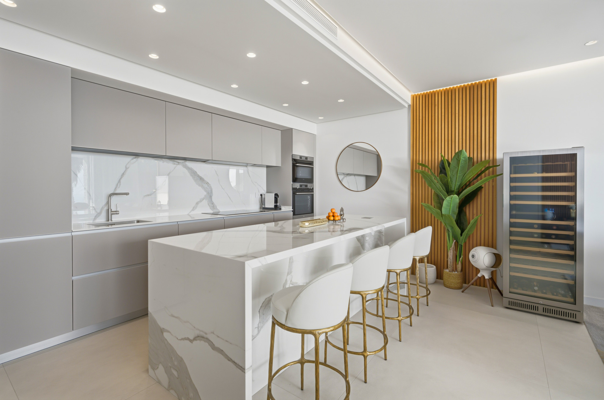 Grey fitted kitchen with a pale veined breakfast island, four stools and a wine cabinet.