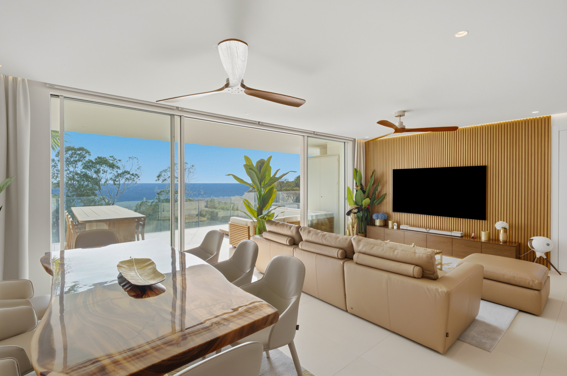 Cream seating, a wood-panelled wall and dining table beside glazing overlooking the terrace and Mediterranean.