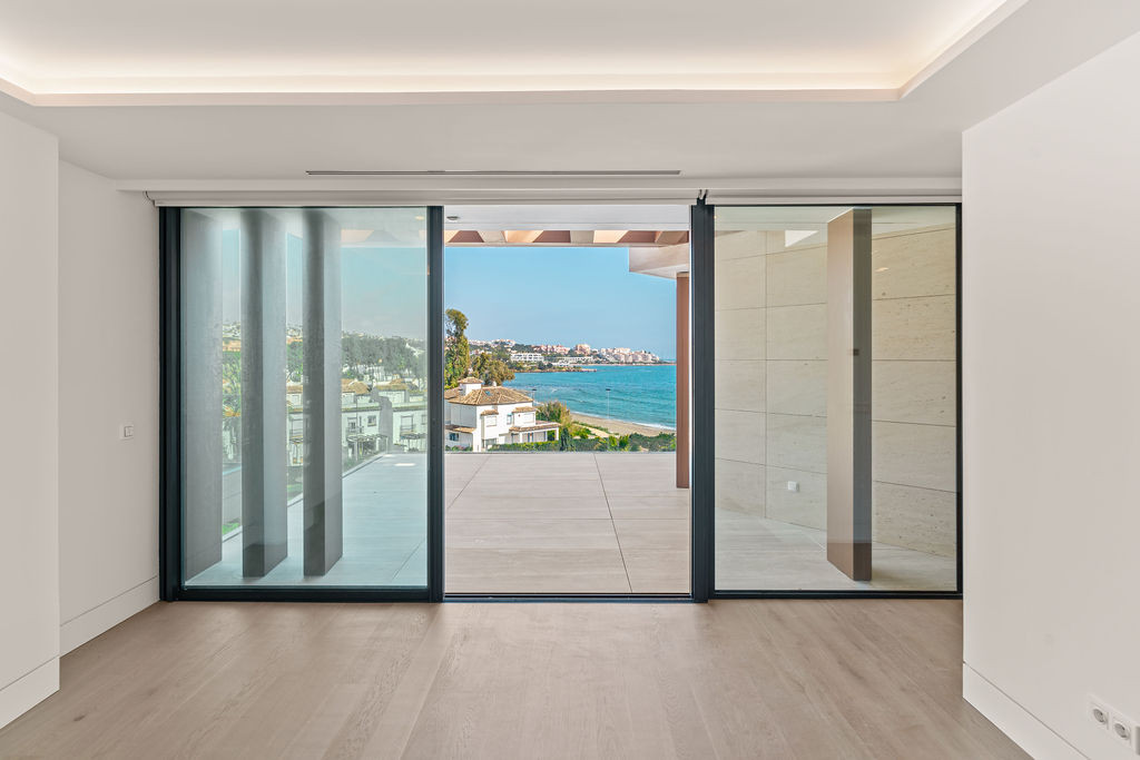 Unfurnished bedroom opening onto a glass-fronted terrace with views towards Estepona